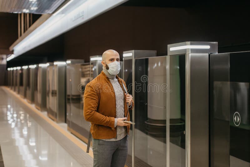 Ein Mann in einer Gesichtsmaske benutzt ein Smartphone, während er auf einen U-Bahn-Zug wartet lizenzfreie stockbilder