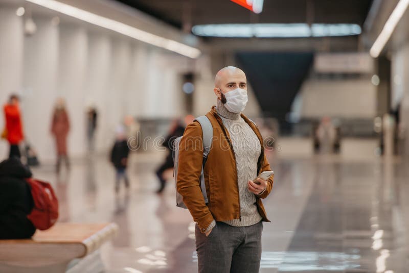 Ein Mann in einer Gesichtsmaske benutzt ein Smartphone, während er auf einen U-Bahn-Zug wartet stockbilder