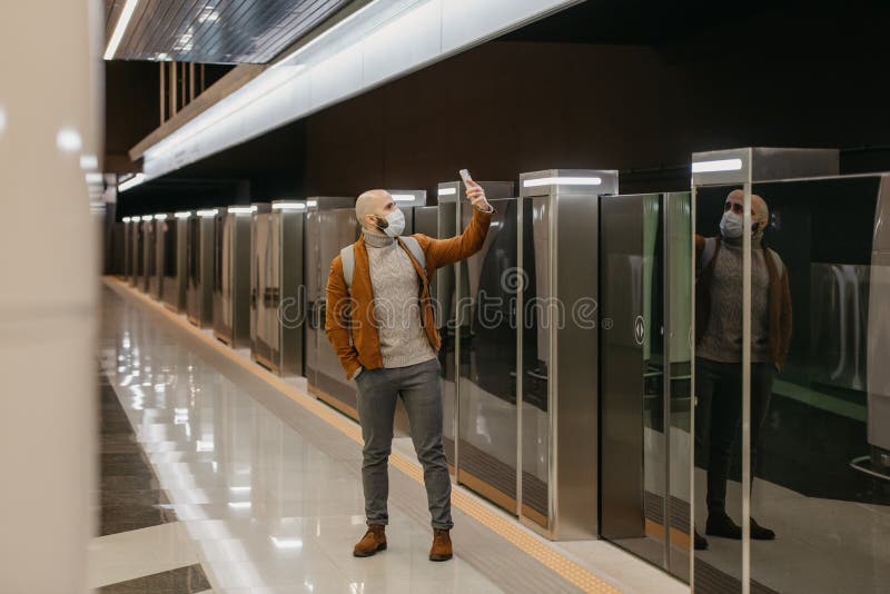 Ein Mann in einer Gesichtsmaske benutzt ein Smartphone, während er auf einen U-Bahn-Zug wartet stockfoto