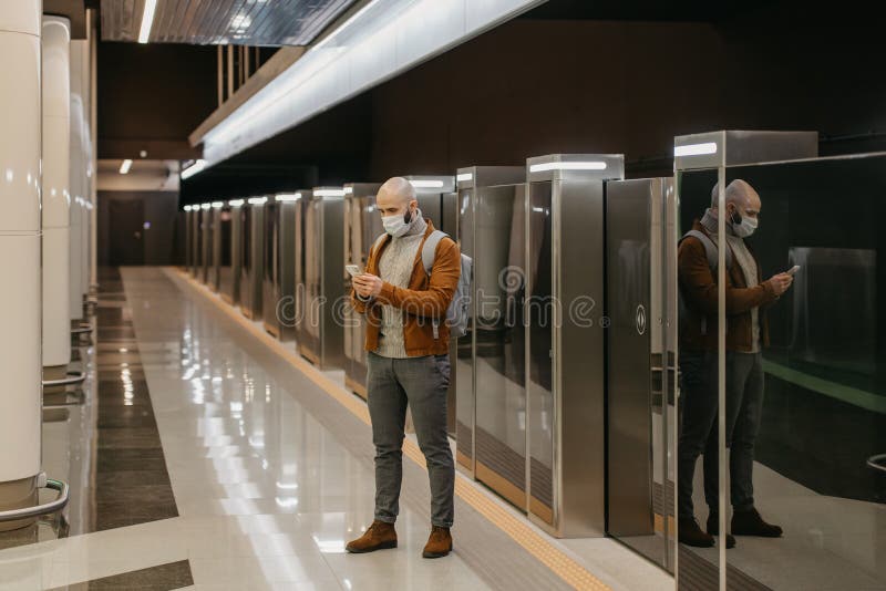 Ein Mann in einer Gesichtsmaske benutzt ein Smartphone, während er auf einen U-Bahn-Zug wartet stockfotografie
