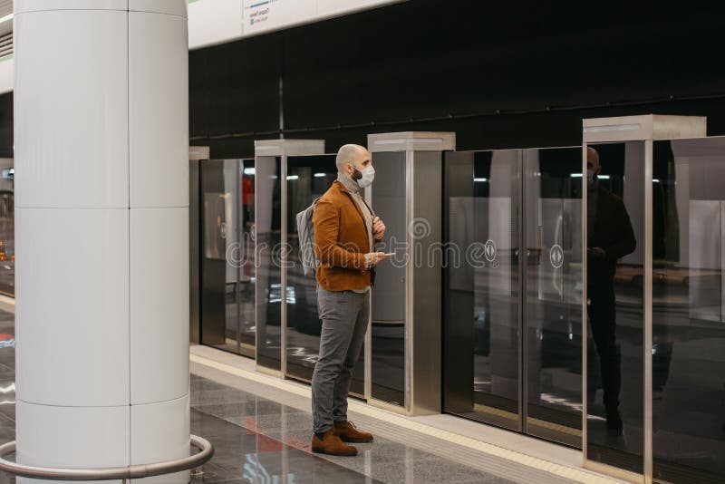 Ein Mann in einer Gesichtsmaske benutzt ein Smartphone, während er auf einen U-Bahn-Zug wartet stockfotos