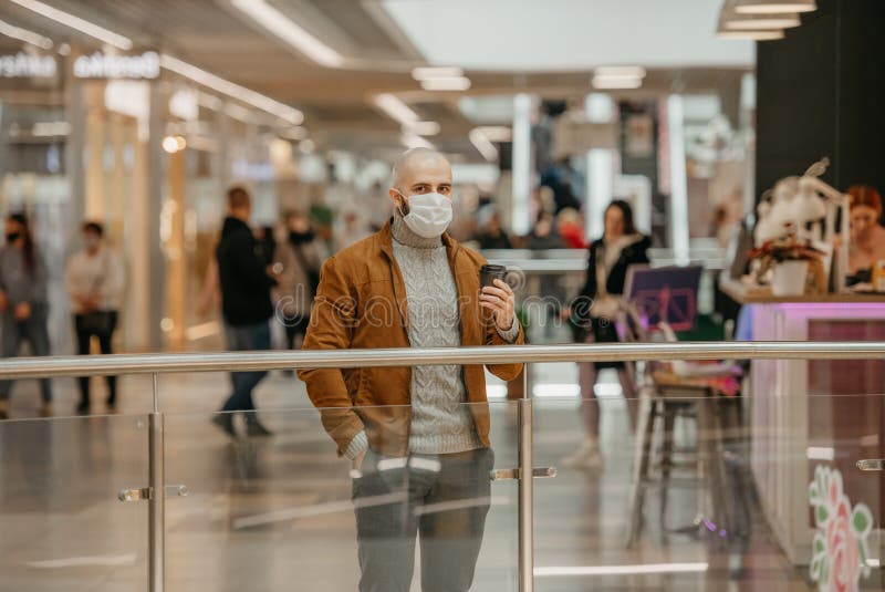 Ein Mann in einer Gesichtsmaske hält eine Tasse Kaffee im Einkaufszentrum lizenzfreies stockbild