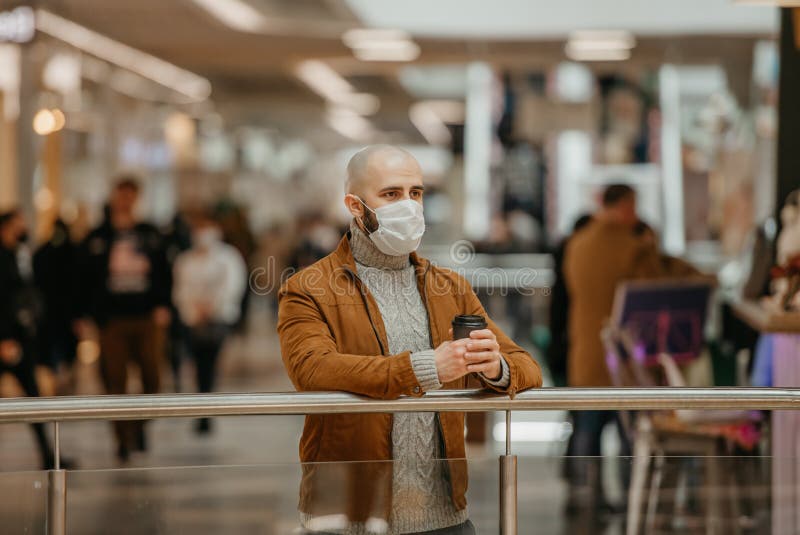 Ein Mann in einer Gesichtsmaske hält eine Tasse Kaffee im Einkaufszentrum stockfoto