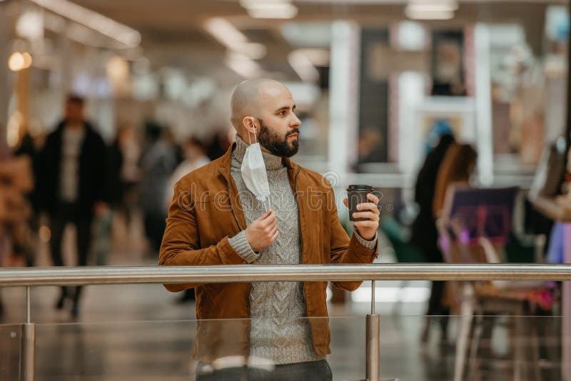 Ein Mann hält eine Abziehmaske, während er im Einkaufszentrum Kaffee trinkt lizenzfreie stockfotos