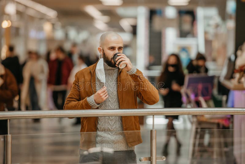 Ein Mann hält eine Abziehmaske, während er im Einkaufszentrum Kaffee trinkt stockfotografie