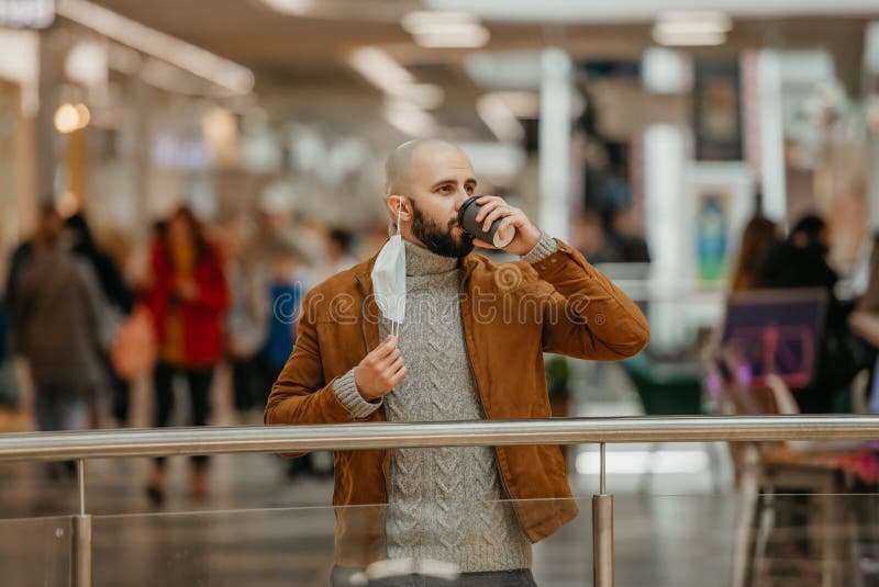 Ein Mann hält eine Abziehmaske, während er im Einkaufszentrum Kaffee trinkt stockfoto