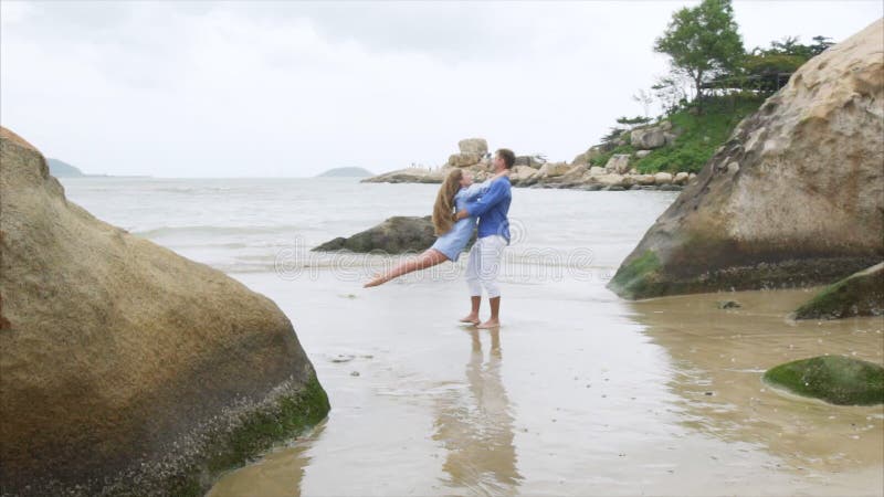 Ein Mann kreist ein Mädchen in seinen Armen auf einem Seesandigen Strand ein Ein Paar des Liebhaberstrudels in der Zeitlupe