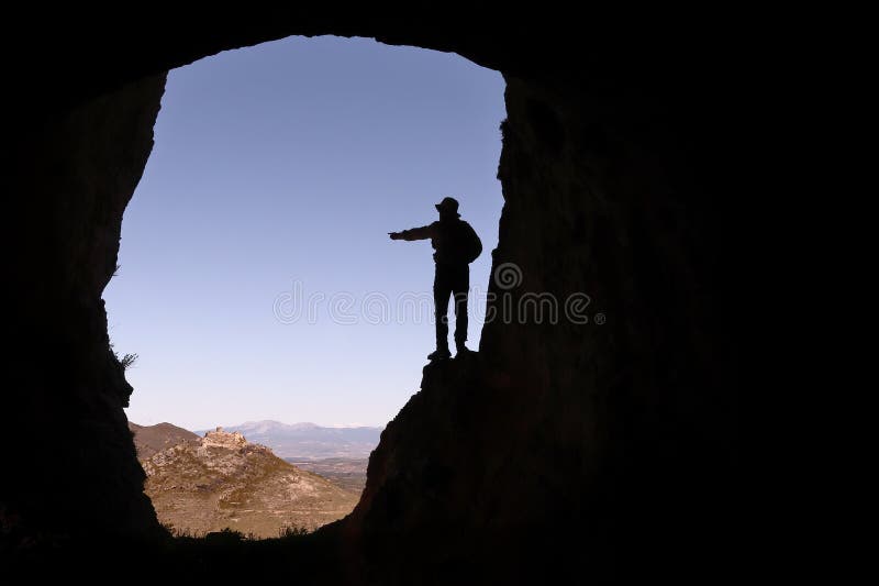 EIN MANN-PFADFINDER MIT EINEM HUT IN EINER HÖHLE ZEIGEND AUF EIN SCHLOSS IM ABSTAND lizenzfreies stockbild