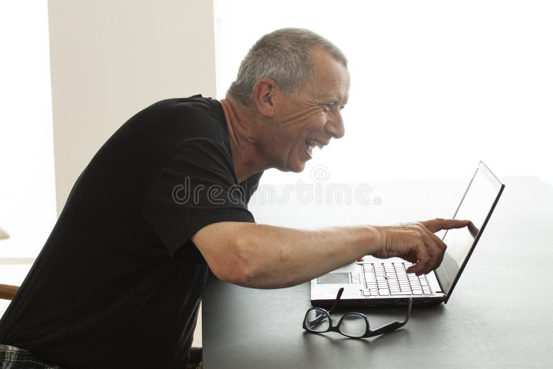 Ein Mann sitzt laut lachen mit offenem Mund, während er auf den Schirm eines Notebooks zeigt Er liest oder sieht lustiges etwas s stockfotografie Ein Mann sitzt laut lachen mit offenem Mund, während er auf den Schirm eines Notebooks zeigt Er liest oder sieht lustiges etwas s stockfotografie