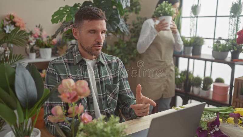 Ein Mann und eine Frau, die in einem üppigen Blumenladen zusammenarbeiten, umgeben von farbenfrohen Blumen und Pflanzen stockbild
