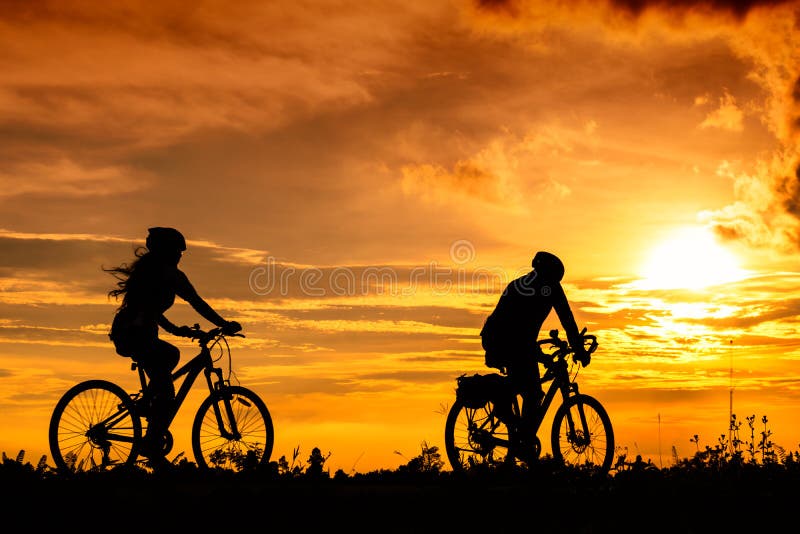 A man and a woman ride bicycles on the road with beautiful colorful sunset sky. Sport and active life concept. A man and a woman ride bicycles on the road with beautiful colorful sunset sky. Sport and active life concept.