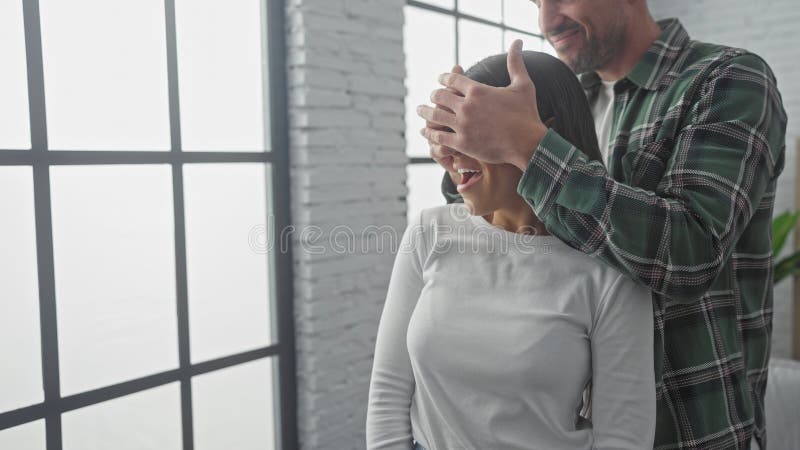 Ein Mann überrascht eine lächelnde Frau drinnen, indem er ihre Augen mit seinen Händen bedeckt und einen spielerischen und liebevo stockfoto