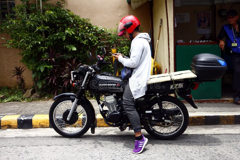 Ein Motorradfahrer stoppt an einem Bürgersteig, um auf seinem Smartphone zu überprüfen lizenzfreie stockbilder Ein Motorradfahrer stoppt an einem Bürgersteig, um auf seinem Smartphone zu überprüfen lizenzfreie stockbilder
