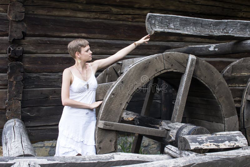 Ein Mädchen in einem weißen Kleid reicht die Hand zu einer hölzernen Struktur mit einem Rad eine alte Wassermühle aus lizenzfreies stockbild