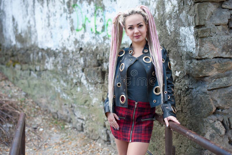 Ein Mädchen mit Dreadlocks in einer Lederjacke und in einem kurzen Rock steht vor dem hintergrund einer alten Steinwand stockfotografie Ein Mädchen mit Dreadlocks in einer Lederjacke und in einem kurzen Rock steht vor dem hintergrund einer alten Steinwand stockfotografie