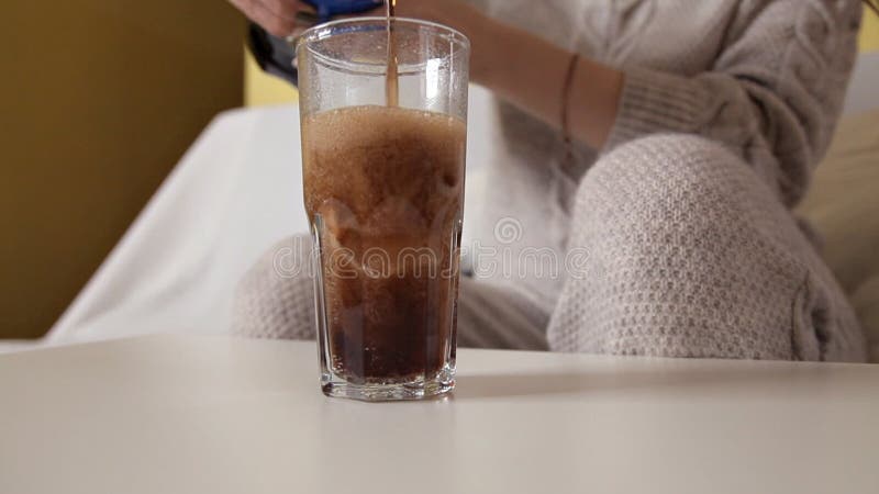 Ein Mädchen sitzt auf einer Couch und gießt einen Kolabaum in ein Glas