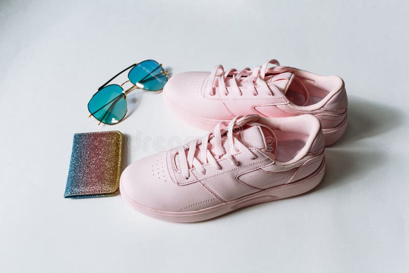 Ein Paar rosa lederne Turnschuhe, Geldbeutel mit mehrfarbigen Pailletten und Sonnenbrille mit blauem Glas auf einem wei?en Hinter lizenzfreies stockbild Ein Paar rosa lederne Turnschuhe, Geldbeutel mit mehrfarbigen Pailletten und Sonnenbrille mit blauem Glas auf einem wei?en Hinter lizenzfreies stockbild