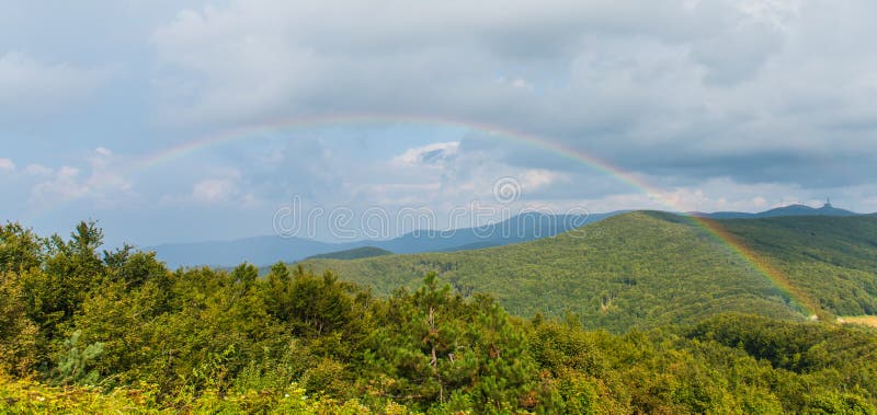 A colorful rainbow over the mountain landscape with trees and mountain peeks on the horizon. A colorful rainbow over the mountain landscape with trees and mountain peeks on the horizon.