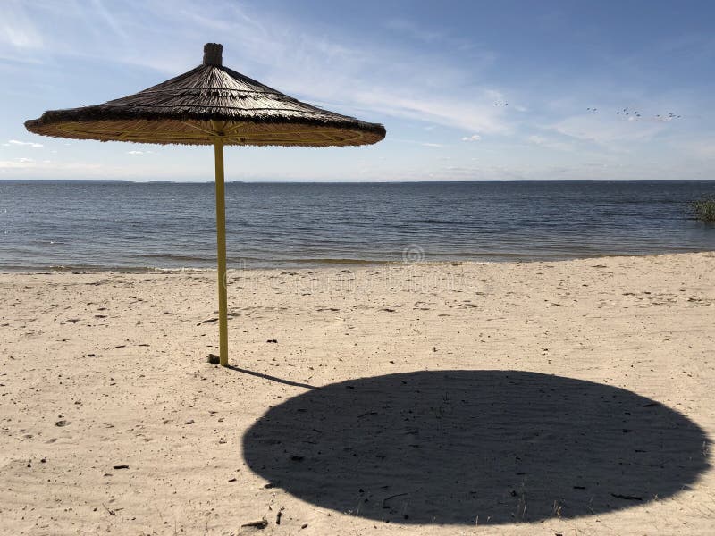 Ein Regenschirm steht auf einem Sandstrand vor dem Hintergrund von Himmel und Wasser Leerer Strand am Ufer eines großen Reservoir stockfotografie
