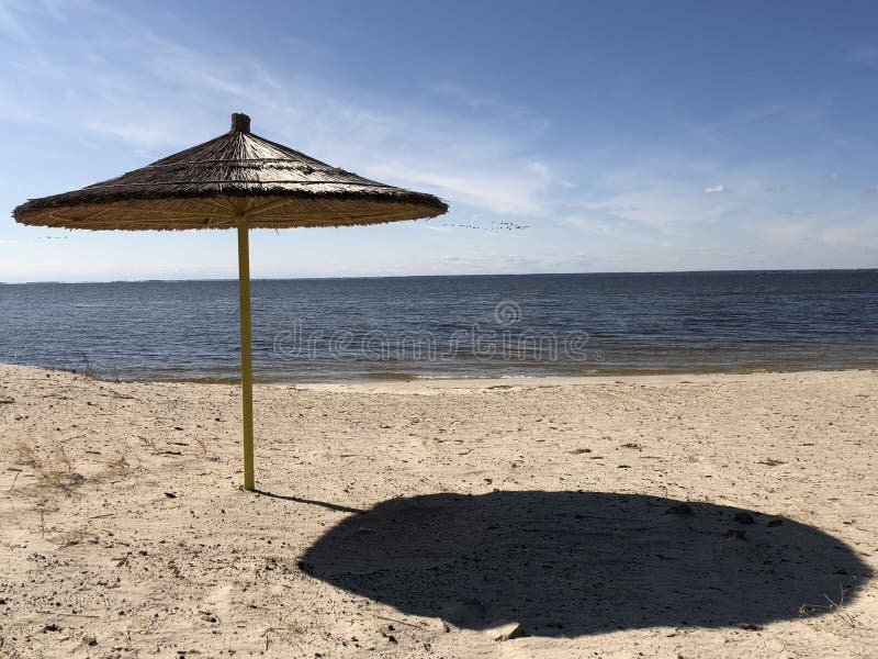 Ein Regenschirm steht auf einem Sandstrand vor dem Hintergrund von Himmel und Wasser Leerer Strand am Ufer eines großen Reservoir lizenzfreies stockfoto