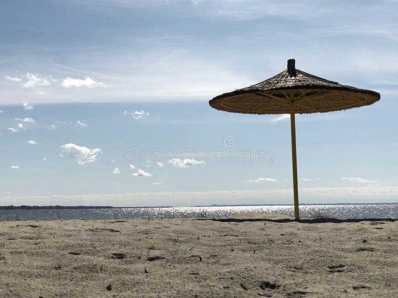Ein Regenschirm steht auf einem Sandstrand vor dem Hintergrund von Himmel und Wasser Leerer Strand am Ufer eines großen Reservoir stockfoto
