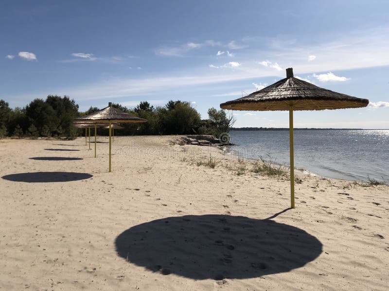 Ein Regenschirm steht auf einem Sandstrand vor dem Hintergrund von Himmel und Wasser Leerer Strand am Ufer eines großen Reservoir stockbilder