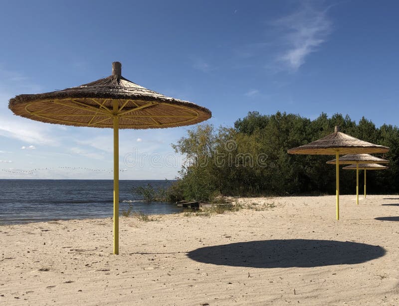 Ein Regenschirm steht auf einem Sandstrand vor dem Hintergrund von Himmel und Wasser Leerer Strand am Ufer eines großen Reservoir stockfoto