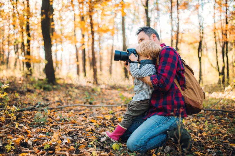 Ein reifer Vater und ein Kleinkindsohn in einem Herbstwald, Fotos mit einer Kamera machend stockbild Ein reifer Vater und ein Kleinkindsohn in einem Herbstwald, Fotos mit einer Kamera machend stockbild