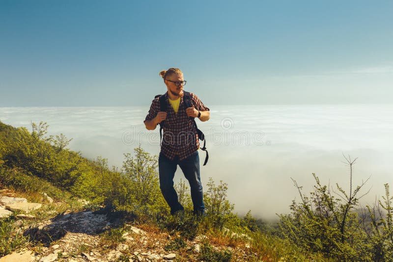 Ein Reisendmann klettert zur Spitze eines Berges gegen einen Hintergrund von Wolken an einem sonnigen Tag Reiselebensstil stockbild
