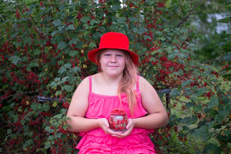 Ein schönes Mädchen in einem hellen Outfit in der Nähe eines roten Johannisbrots. lizenzfreies stockfoto