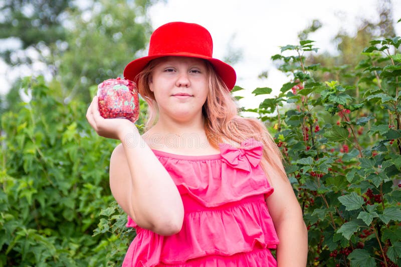 Ein schönes Mädchen in einem hellen Outfit in der Nähe eines roten Johannisbrots. lizenzfreie stockfotos