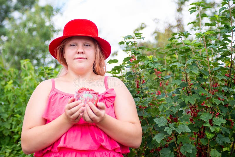 Ein schönes Mädchen in einem hellen Outfit in der Nähe eines roten Johannisbrots. lizenzfreies stockbild