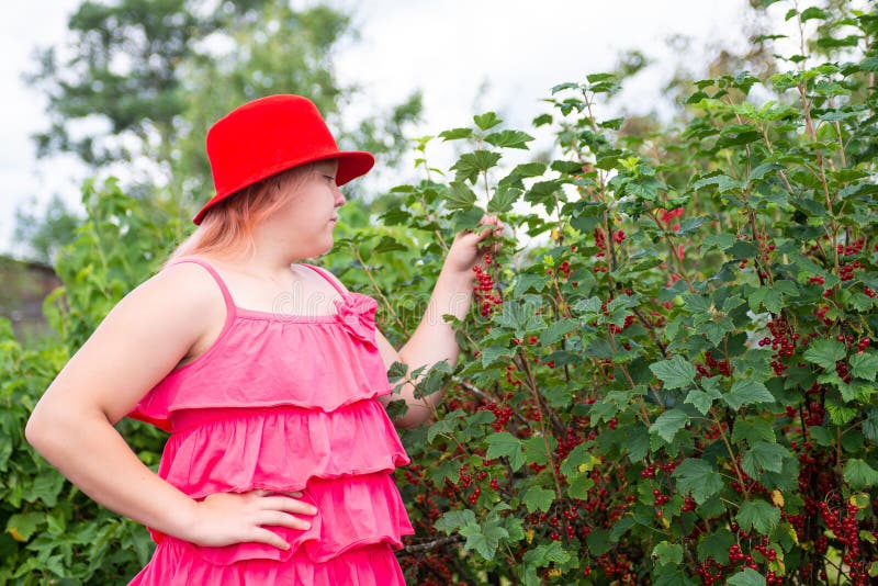 Ein schönes Mädchen in einem hellen Outfit in der Nähe eines roten Johannisbrots. lizenzfreie stockfotos