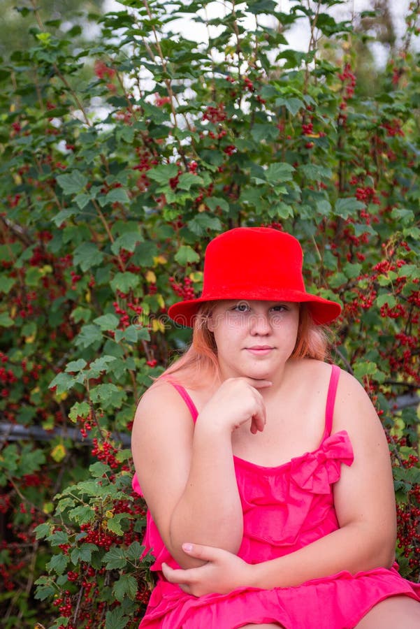 Ein schönes Mädchen in einem hellen Outfit in der Nähe eines roten Johannisbrots. stockfoto