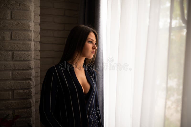 Ein sexy Mädchen in einem ungeknöpften Hemd steht in der Nähe des Fensters lizenzfreie stockfotos