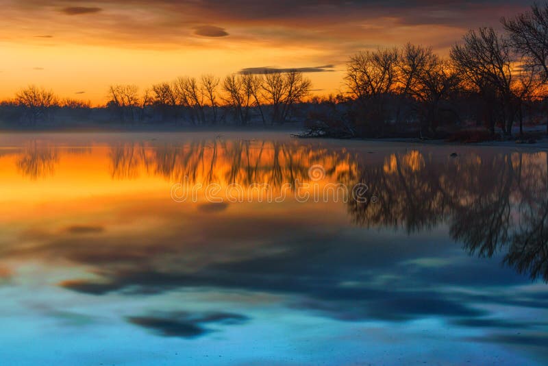 Sunrise lights up the sky over Lake Ladora in Denver, Colorado on a morning in late Fall. Sunrise lights up the sky over Lake Ladora in Denver, Colorado on a morning in late Fall