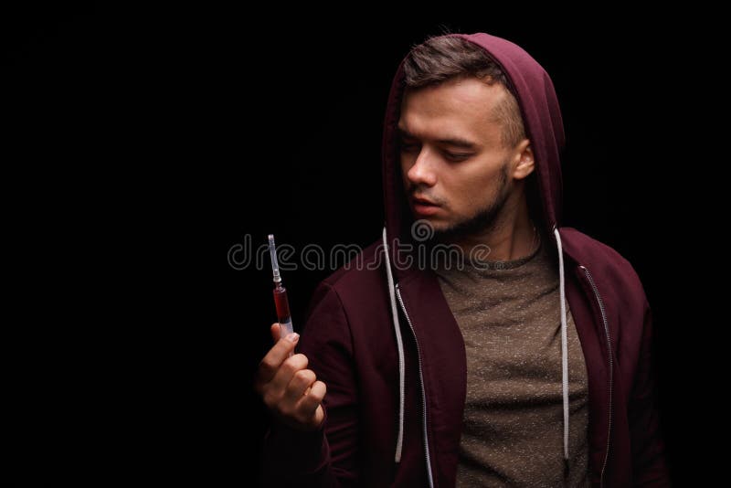 Ein süchtiger Junkie in einem purpurroten Sweatshirt leidet unter Drogensucht mit einer Spritze in einer Hand auf einem schwarzen stockbilder Ein süchtiger Junkie in einem purpurroten Sweatshirt leidet unter Drogensucht mit einer Spritze in einer Hand auf einem schwarzen stockbilder