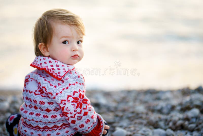 Ein süßes kleines Mädchen auf einem schönen Pullover am Ufer des Wintermeeres, das mit süßen Augen in die Kamera verwandelt wurde lizenzfreies stockbild