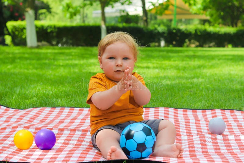 Ein süßes Kleinkind sitzt an einem Sommertag auf einer Decke und klatscht sich. Fokus auf Kinderkonzept. Spaß stockfoto