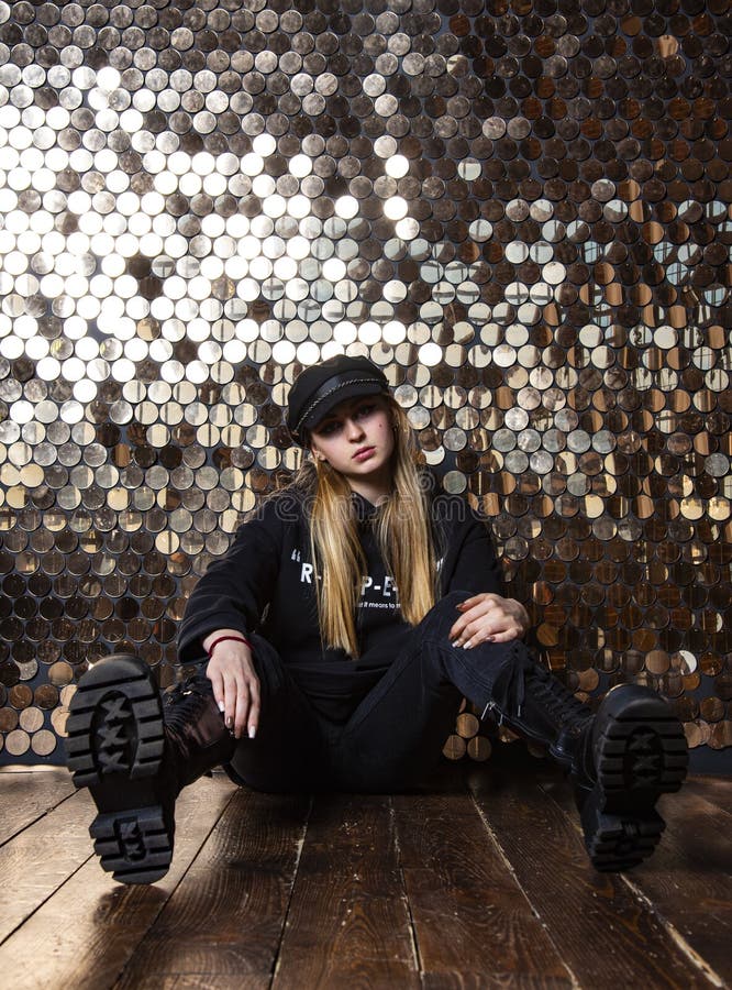 Ein Teenager in schwarzer Kleidung sitzt an einer goldenen Wand. lizenzfreies stockbild