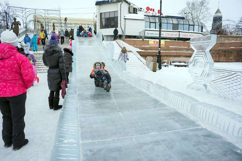 Ein Vati mit einem Kind in seinen Armen rollt unten einen eisigen Hügel in der Mitte von Krasnojarsk während der Winter Neujahrsf stockfoto Ein Vati mit einem Kind in seinen Armen rollt unten einen eisigen Hügel in der Mitte von Krasnojarsk während der Winter Neujahrsf stockfoto