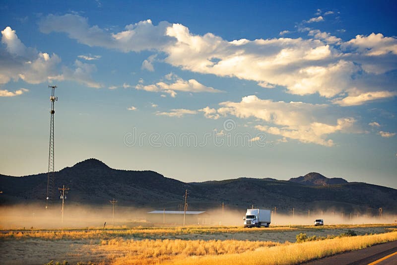 Ein Weisser Lkw Auf Einer Staubigen Autobahn Im Hintergrund Sind Dunkelbraune Hugel Und Ein Dunkelblauer Himmel Mit Flaumigen Wolk Stockbild Bild Von Staubigen Hintergrund