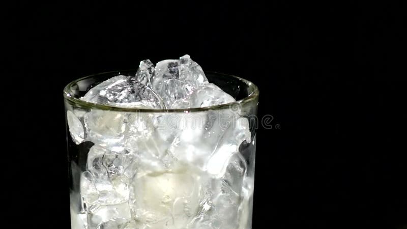 Ein Würfel des Eises fallend in ein Glas Wasser abschluß