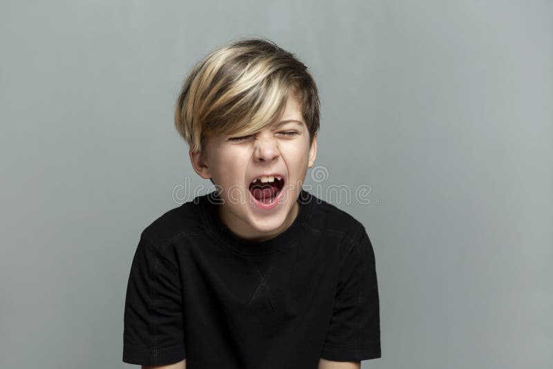 Ein 9yearold Junge in einem schwarzen T-Shirt schreit.. Kriseneinsamkeit und -Lernschwierigkeiten. grauer Hintergrund