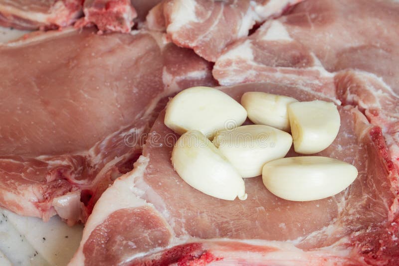 Eine Absperrung mit einer Handvoll Knoblauchblüten auf einem rohen Schweinekopf mit Salz auf einem Brett stockbild