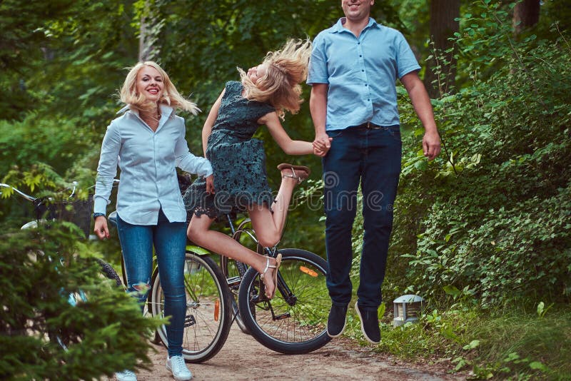 Eine attraktive Familie kleidete in der zufälligen Kleidung auf einer Fahrradfahrt an, hat Spaß und das Springen in einem Park stockfoto Eine attraktive Familie kleidete in der zufälligen Kleidung auf einer Fahrradfahrt an, hat Spaß und das Springen in einem Park stockfoto