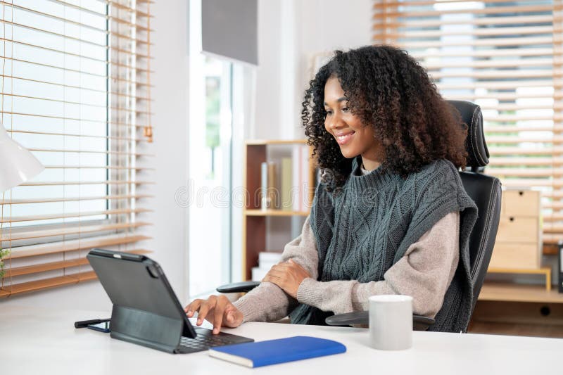Eine attraktive schwarze Frau arbeitet in ihrem privaten Büro und benutzt ihre digitale Tablette am Schreibtisch lizenzfreie stockbilder