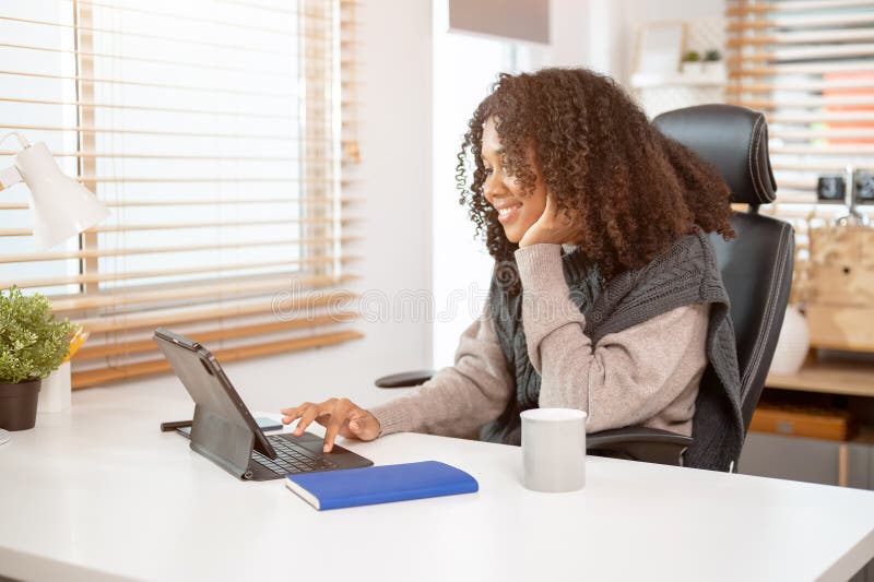 Eine attraktive schwarze Frau arbeitet in ihrem privaten Büro und benutzt ihre digitale Tablette am Schreibtisch stockfotografie