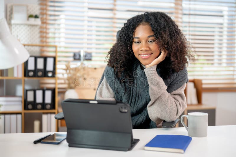 Eine attraktive schwarze Frau arbeitet in ihrem privaten Büro und benutzt ihre digitale Tablette am Schreibtisch lizenzfreie stockfotografie