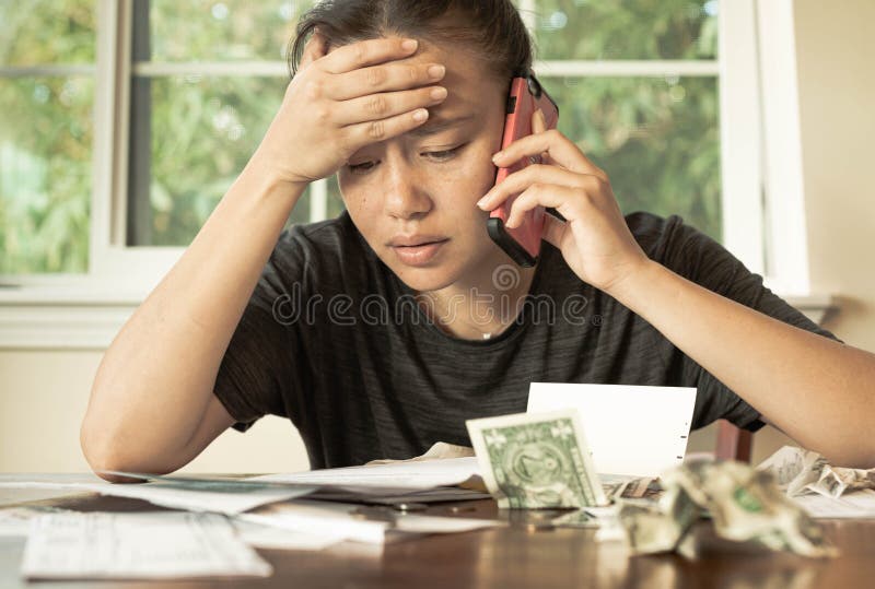 Poor person sitting at the table at home looking over all her bills and credit card fees with 1 dollar bills and coins lying around, stressed worried look on her face. Poor person sitting at the table at home looking over all her bills and credit card fees with 1 dollar bills and coins lying around, stressed worried look on her face